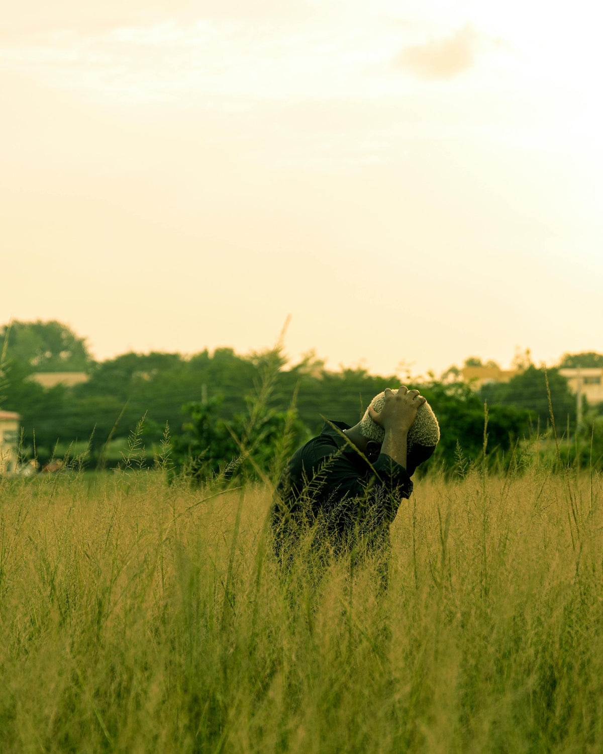 A figure standing in tall grass at sunset.