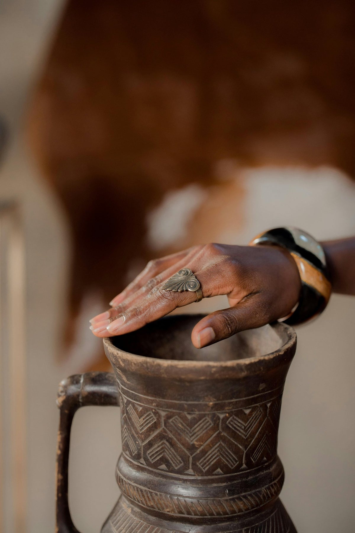 A hand resting on the lid of a carved wooden pot.